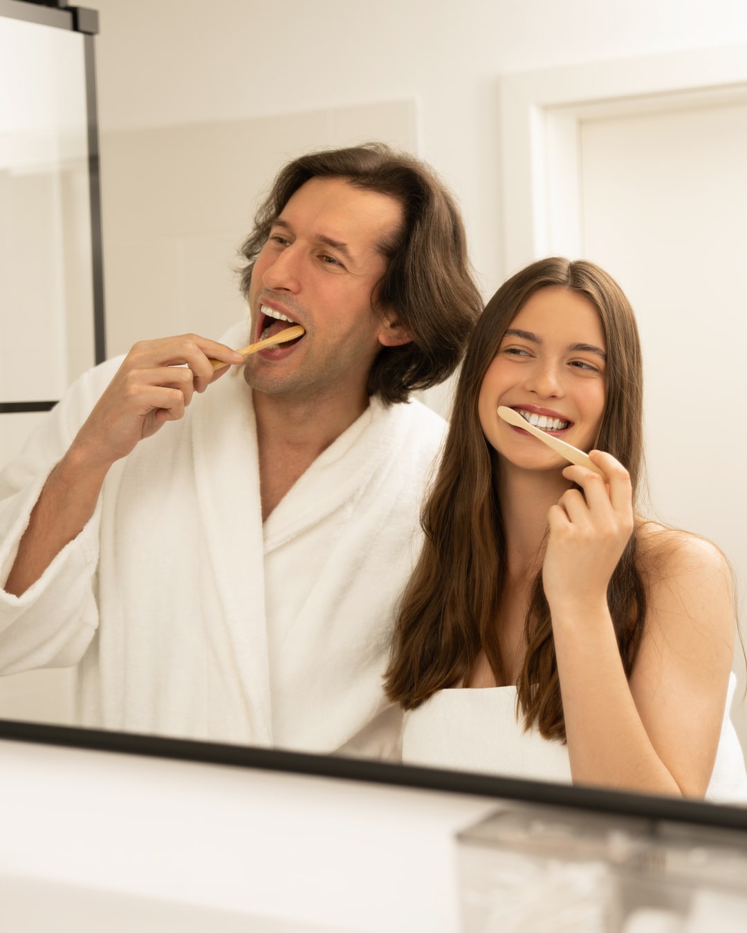 Lächelndes Paar putzt sich gemeinsam mit Bambuszahnbürsten und Zahnaufhellungspulver im Badezimmer die Zähne