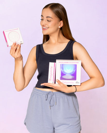 Junge Frau hält das Zahnaufhellungssystem mit LED-Lampe, eine Packung Zahnaufhellungspulver und eine Tube Whitening-Gel von OnlySmile – Komplettset für Zahnaufhellung