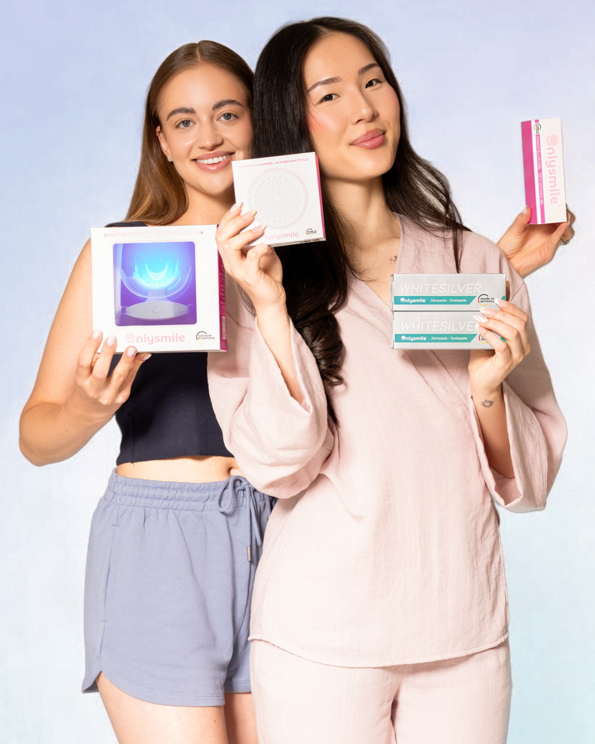 Zwei Frauen präsentieren ein Zahnaufhellungs-Set, Zahnaufhellungspulver, ein Whitening-Gel und zwei Zahnpasten von OnlySmile