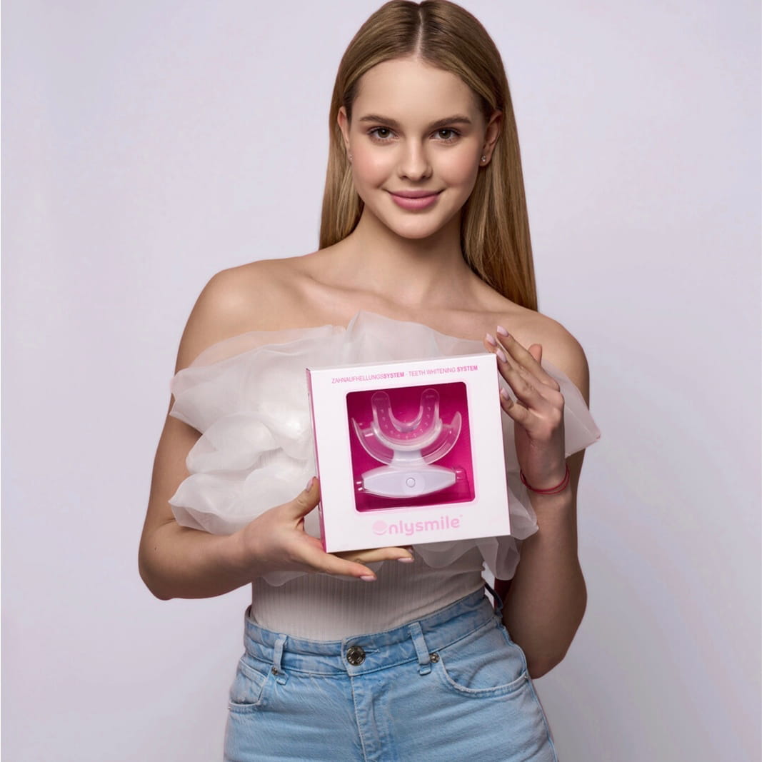 Junge Frau präsentiert ein OnlySmile Zahnaufhellungsset mit LED-Zahnschiene vor hellem Studiohintergrund.