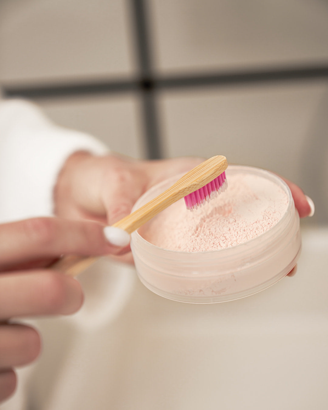 Bambuszahnbürste wird in rosa Zahnaufhellungspulver getaucht – Nahaufnahme der Anwendung